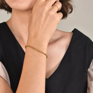 Primo piano di un bracciale a sfere dorate e anello solitario indossati su un polso femminile