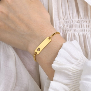 Detailed close-up of a golden box chain bracelet with a cutout heart rectangular ID plate