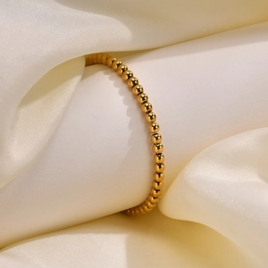 Detailaufnahme eines goldenen Edelstahl-Perlenarmbands auf einem weißen Seidendisplay
