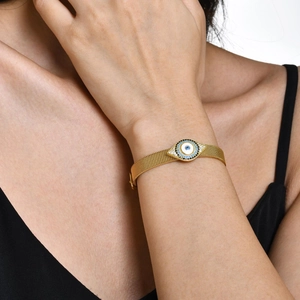 Détail macro du bracelet à mailles dorées orné d'une breloque œil porte-bonheur et cristaux