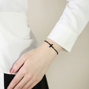 Detail shot of a minimalist black stainless steel cross bracelet on a model's wrist