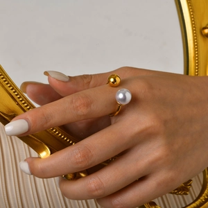 Détail d'une bague ouverte dorée avec perle blanche et bille métallique polie à la main