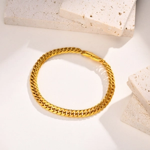 Détail d'un bracelet gourmette dorée sur du marbre blanc avec une texture naturelle