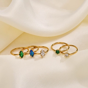 Close-up of five gold rings set with green, blue, and white marquise-cut zircons