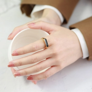 Gros plan d'une bague géométrique dorée avec insert noir portée sur une main avec tasse