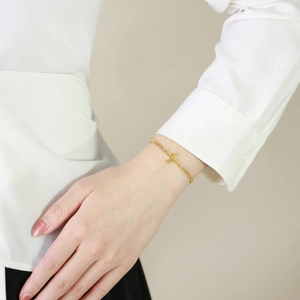 Detail of a delicate gold-plated cross bracelet worn on a woman's wrist with a white shirt