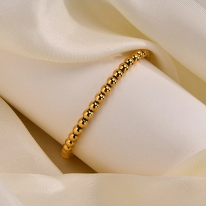 Poliertes goldenes Kugelarmband auf weißem Seidenhintergrund mit elegantem Faltenwurf