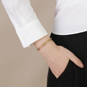 Gros plan d'un bracelet à maillons trombone dorés porté au poignet avec élégance