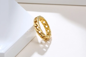 Détail d'une bague chaîne cubaine dorée en acier inoxydable sur un support blanc