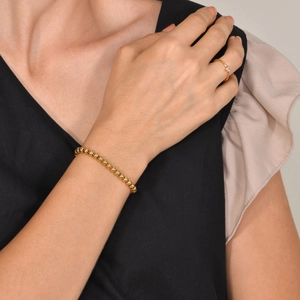 Primo piano del bracciale di perline dorate e dell'anello con zircone sul polso e dito