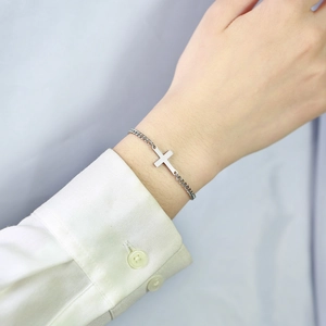 Close-up of a minimalist silver stainless steel cross bracelet worn on a female wrist