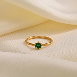 Macro detail of gold ring featuring a hexagonal green zircon set on satin background
