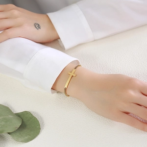 Detail of gold box chain bracelet with horizontal cross pendant on female wrist