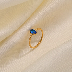 Close-up of gold ring with marquise-cut blue zircon on soft beige silk fabric