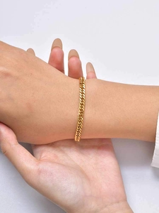 Gros plan d'un bracelet gourmette en or porté au poignet avec des maillons plats