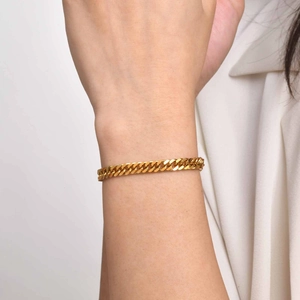 Gros plan d'un bracelet gourmette en acier inoxydable doré porté sur le poignet d'une personne