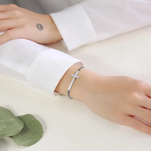 Polished silver stainless steel cross bracelet on a female wrist with minimalist styling