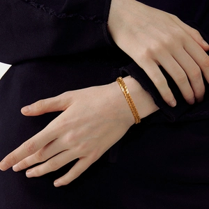 Détail macro d'un bracelet gourmette doré poli sur poignet avec fond sombre contrasté