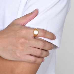 Close-up of golden signet ring with white oval shell inlay on woman's finger