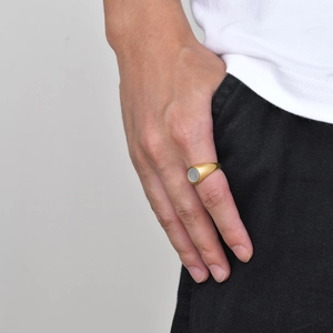Close-up of a gold stainless steel signet ring with a round white shell inlay on model hand