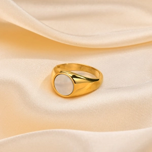 Detailed view of gold signet ring with white shell inlay on champagne satin background