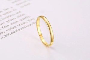 Detailed side view of a minimalist thin gold band ring on a neutral book background