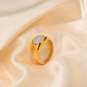 Detailed shot of golden stainless steel ring with white shell inlay on silk fabric