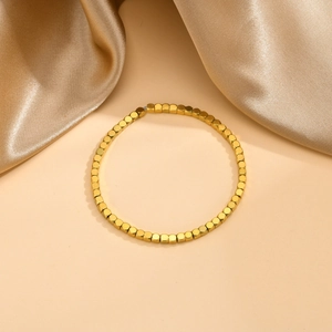 Gros plan du bracelet à billes carrées dorées sur un fond élégant en satin champagne