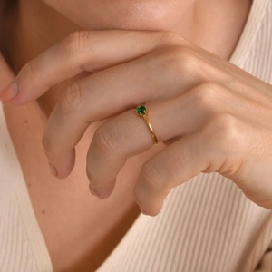 Close-up of minimalist gold ring with small green zircon on female index finger