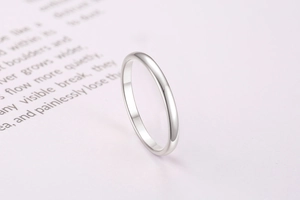 Macro detail of polished silver stainless steel band ring on minimalist paper background