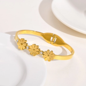 Détail d'un bracelet doré avec breloques marguerites et cristaux de zircon sur céramique blanche