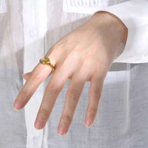 Gold oval stainless steel ring with sunburst texture worn on a hand over a white shirt