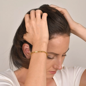 Gros plan d'un bracelet à perles dorées porté par un mannequin en tenue blanche chic