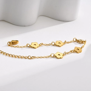 Détail d'un bracelet doré poli avec cinq pendentifs fleurs évidés sur une chaîne à maillons