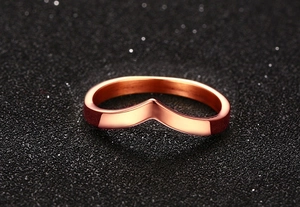 Close-up of a polished rose gold V-shaped chevron ring on a dark textured background