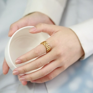 Detail of a gold watch-band style hollow mesh ring worn on a finger with a clean aesthetic