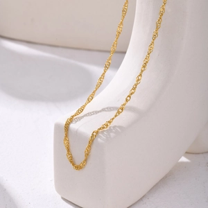 Macro view of gold minimalist water wave twist chain necklace on white display stand