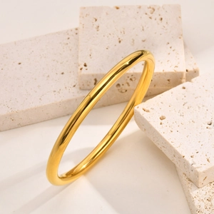 Close-up of a high-polished gold titanium steel bangle on a textured stone surface