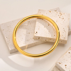 Minimalist gold titanium steel bangle bracelet displayed on a natural beige stone prop
