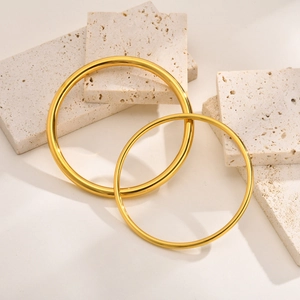 Polished 304 stainless steel gold bangles displayed on neutral travertine stone tiles