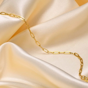 Detailaufnahme des goldenen Büroklammer-Armbands auf elegantem champagnerfarbenem Seidenstoff