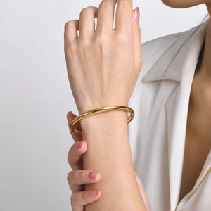 Minimalist gold titanium steel bangle on model wrist with elegant white suit background