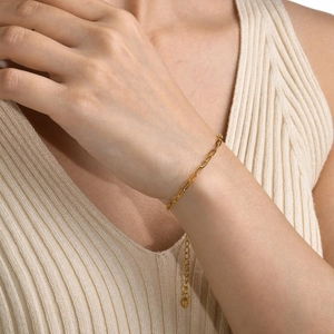 Detail eines goldenen Büroklammer-Kettenarmbands am Handgelenk vor Strickhintergrund