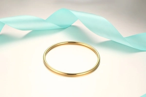 Close-up of a minimalist polished gold titanium steel bangle with blue silk ribbon decor