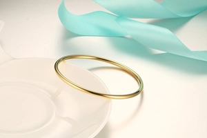 Close-up of minimalist gold titanium steel bracelet on ceramic tray with blue silk ribbon