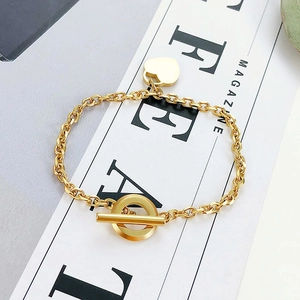 Dettaglio del bracciale dorato con ciondolo a cuore e chiusura OT su sfondo rivista