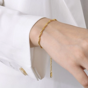 Elegant gold twisted rope chain bracelet for women on a white suit cuff background
