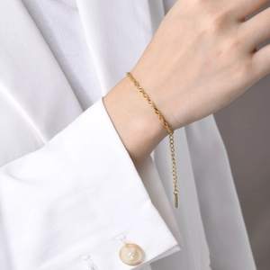 Detail of golden water wave chain bracelet on a wrist with a white suit sleeve