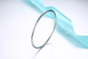 Polished stainless steel bangle on soft blue silk ribbon background with mirror finish