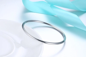 Minimalist high-polished gold stainless steel bangle on a white ceramic plate with blue ribbon
